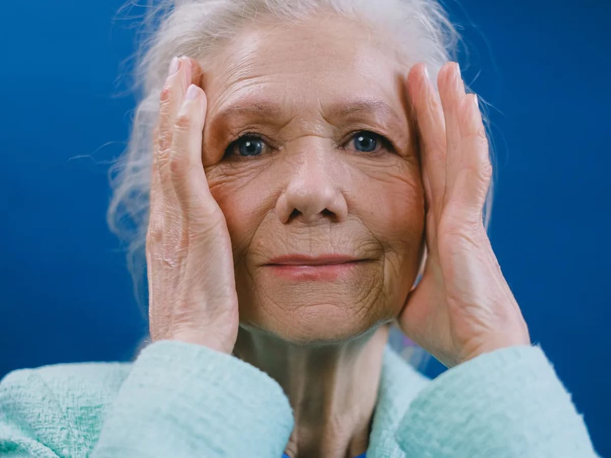Mature woman with fine lines around her eyes, smiling with her hands on her face
